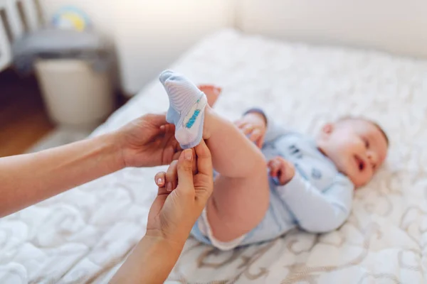 ケアの母親の赤ちゃんの足に小さな靴下を置くのを閉じる ベッドの上に寝そべって徒歩での選択的フォーカス — ストック写真