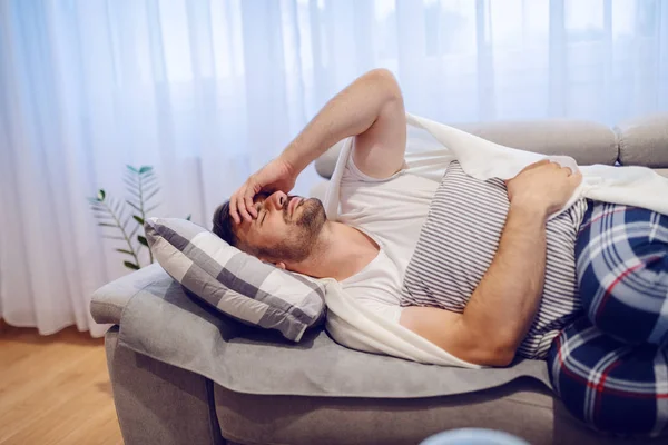 身穿睡衣的英俊的高加索男人躺在客厅的沙发上 肚子痛 — 图库照片