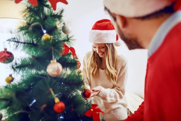 Förtjusande Kaukasiska Par Dekorera Julgran Båda Har Tomtehattar Huvudet Vardagsrum — Stockfoto