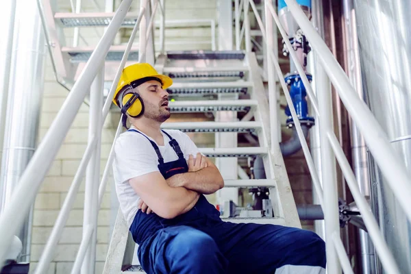 Müder Fabrikarbeiter Overalls Mit Schutzhelm Und Antiphonen Auf Treppen Sitzend — Stockfoto