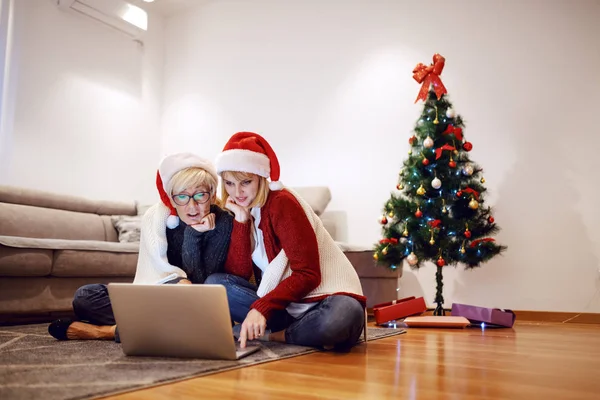 아름다운 금발의 어머니와 바닥에 노트북을 사용하고 있습니다 머리에 모자를 배경에는 — 스톡 사진
