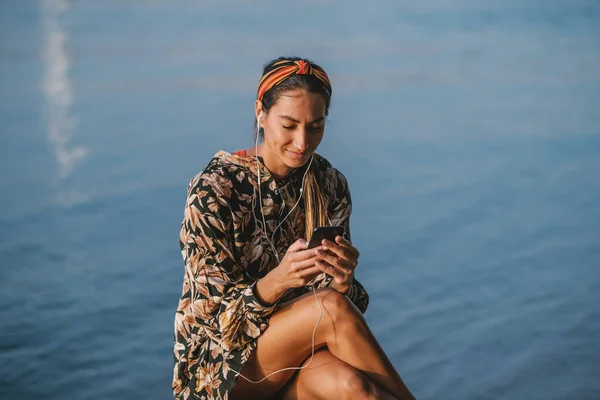 Çiçekli Elbiseli Başında Bantla Nehir Kıyısında Oturan Akıllı Telefon Kullanan — Stok fotoğraf