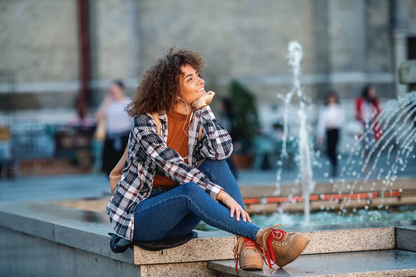 年轻迷人的混血女子坐在喷泉上欣赏音乐 — 图库照片