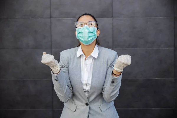 Young attractive businesswoman with protection mask and gloves on celebrating success. Protection form corona virus concept.