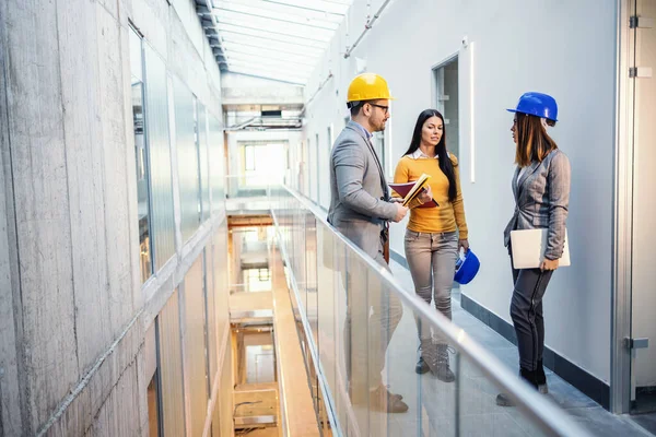 Three architects standing inside of future business center and talking about renewal.