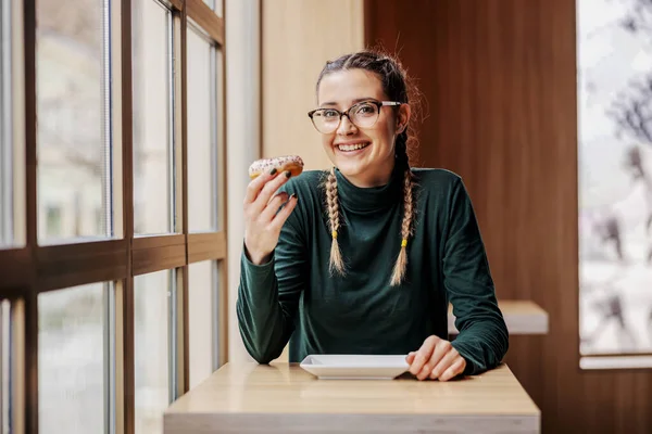 Mulher Sorridente Atraente Sentado Cafetaria Segurando Donut Desfrutando Tempo Livre — Fotografia de Stock