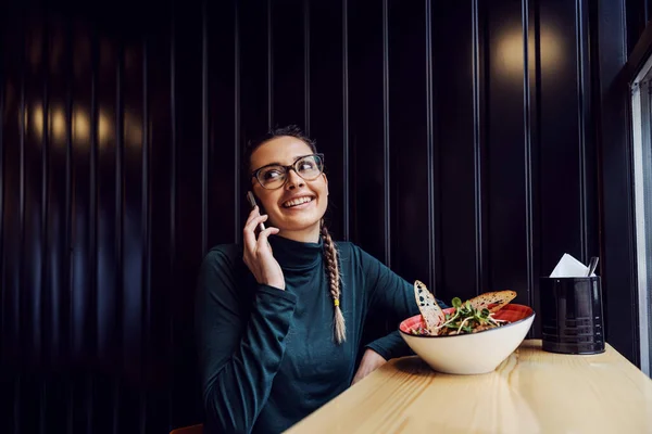Gülümseyen Kadın Pencerenin Yanındaki Restoranda Oturuyor Arkadaşlarıyla Telefon Görüşmesi Yapıyor — Stok fotoğraf