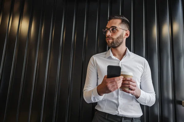 Joven Hombre Guapo Pie Interior Sosteniendo Teléfono Inteligente Café Fresco — Foto de Stock