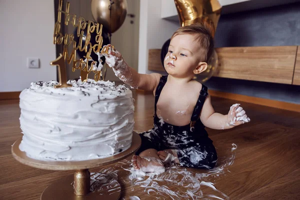Cute little baby boy sitting on the floor and playing with his cake on his first birthday.