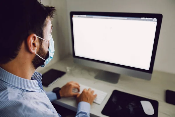 雇员坐在办公室里 戴着面具 在日冕爆发时使用笔记本电脑的后视镜 — 图库照片