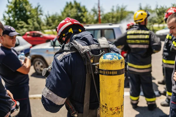 他の消防士のグループに消防士が立って 彼の背中に消火器を持っています 彼は行動の準備をしている — ストック写真