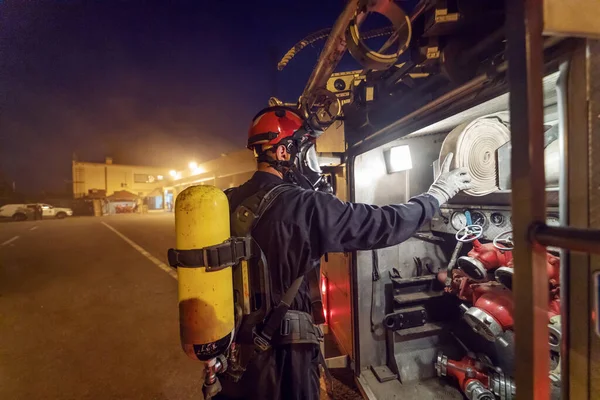 夜に火を消すために消防車からホースを取って保護制服や完全な機器で勇敢な消防士 — ストック写真