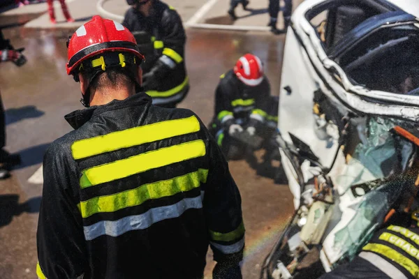 消防士は墜落した車から男を解放しようとしてる 事故で墜落した車がある — ストック写真