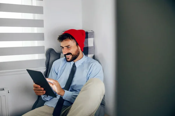 턱수염웃는 사업가가 사무실에서 멈추어 노트북을 사용하면서 머리에 모자를 사무실에 — 스톡 사진