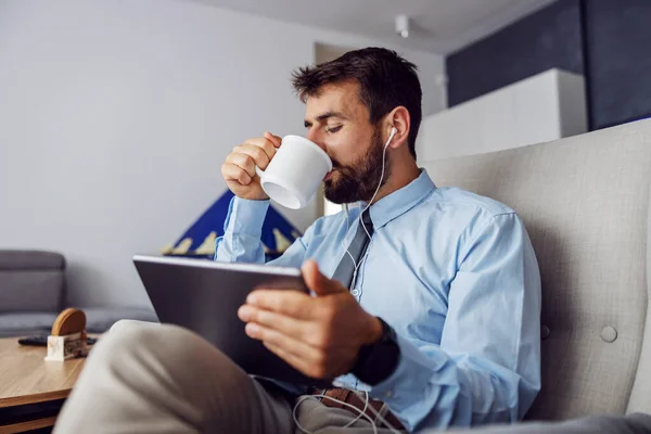 Όμορφος Γενειοφόρος Επιχειρηματίας Πίνοντας Καφέ Και Χρησιμοποιώντας Tablet Ενώ Κάθεται — Φωτογραφία Αρχείου