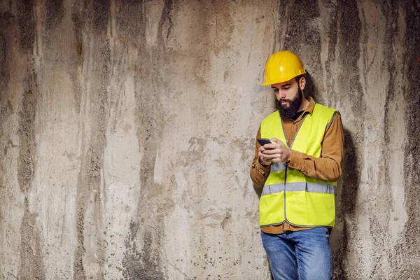 Genç Yakışıklı Sakallı Işçi Beton Duvarın Önünde Duruyor Akıllı Telefon — Stok fotoğraf