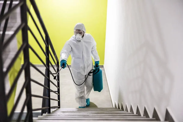 穿着防护服和面罩的工人用电晕病毒 19对建筑物的栏杆进行灭菌 — 图库照片