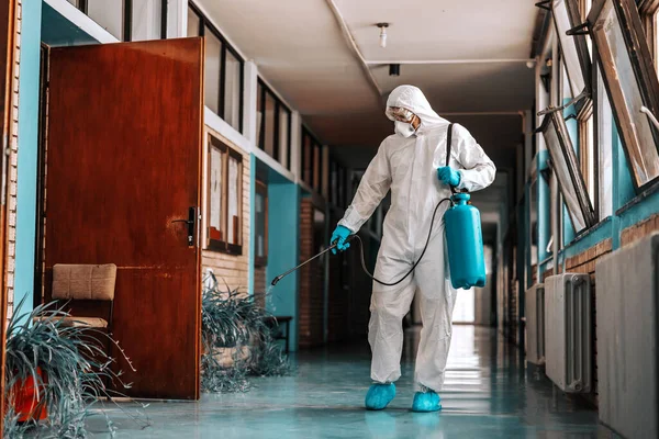穿着消毒制服的工人 戴着橡胶手套 拿着装有消毒剂的喷雾器 并在学校走廊内喷洒 — 图库照片