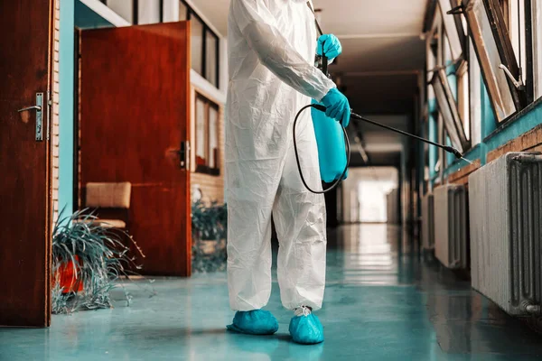 穿着消毒制服的工人 戴着橡胶手套 拿着装有消毒剂的喷雾器 并在学校走廊内喷洒 — 图库照片