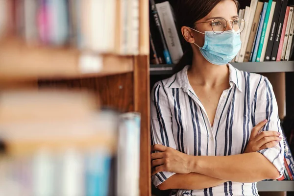 얼굴에 마스크를 매력적 신입생이 시선을 돌리며 도서관에 있습니다 코로나 바이러스 — 스톡 사진