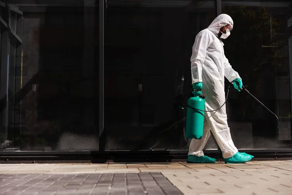 ゴム手袋と滅菌保護制服の人間の側面図消毒剤で噴霧器を保持し コロナウイルスのフォームが広がるのを防ぐために屋外に噴霧 — ストック写真