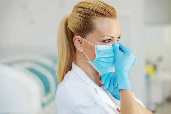 带着橡胶手套站在医院并戴上无菌面罩的漂亮金发实验室助理的画像 — 图库照片