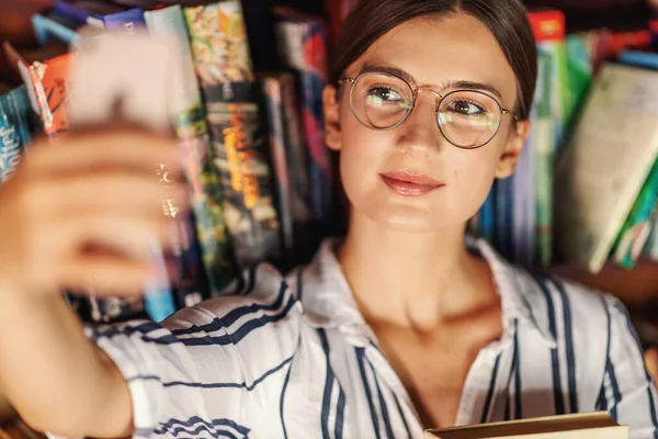 Zbliżenie Młoda Piękna Brunetka Stojąc Bibliotece Trzymając Książkę Biorąc Selfie — Zdjęcie stockowe