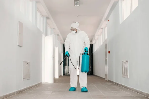 身穿无菌制服 戴口罩 手持喷洒消毒剂和喷洒学校走廊的工人全长 — 图库照片