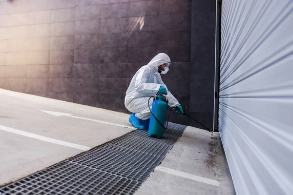 ゴム手袋を身に着けている滅菌保護制服の男がコロナウイルスの拡散を防ぐために消毒剤ガレージドアでうずき — ストック写真