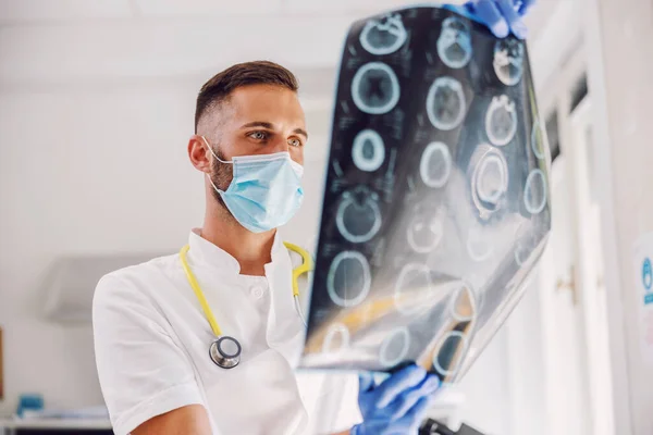 Vonzó Elkötelezett Fiatal Orvos Áll Kórházban Arcmaszkkal Gumikesztyűvel Nézi Röntgen — Stock Fotó
