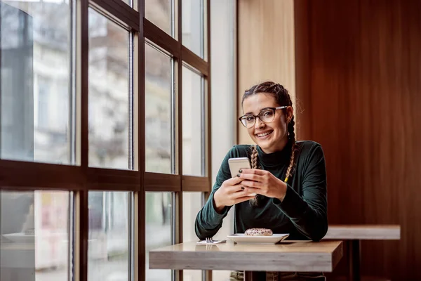 Joven Mujer Sonriente Sentada Cafetería Sosteniendo Teléfono Inteligente Mirando Cámara — Foto de Stock