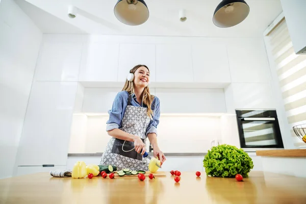 Jovem Mulher Caucasiana Feliz Avental Cozinha Cortar Pimenta Enquanto Ouve — Fotografia de Stock