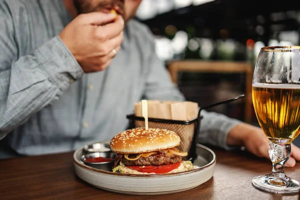 中年の髭を生やした空腹の男がレストランに座っておいしいハンバーガーを食べて — ストック写真