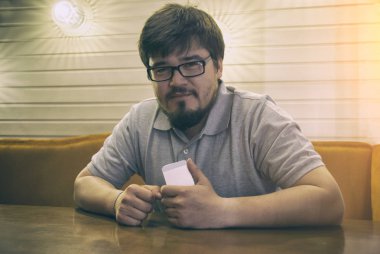 Genç sakallı adam gözlük ve gri gömlek oturma içinde bar telefon ve sana bakıyor. Adam akıllı telefon ile el sevindim