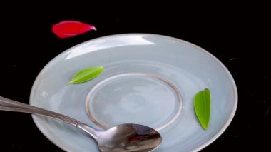 4k video Yeşil yaprak ve kırmızı gül yaprağı ile siyah arka plan üzerinde bir kaşık ile mavi bir kahve fincanı bir yudum alma ve daha sonra döşeme