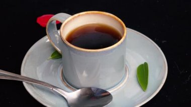 4k video Yeşil yaprak ve kırmızı gül yaprağı ile siyah arka plan üzerinde bir kaşık ile mavi bir kahve fincanı bir yudum alma