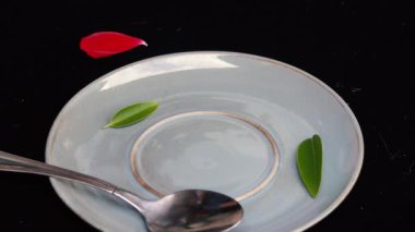 4k video Yakın karıştırın veya yeşil yaprak ve kırmızı gül yaprağı ile siyah arka plan üzerinde bir kaşık ile mavi bir kahve fincanı karıştırma ve daha sonra aşağı döşeme