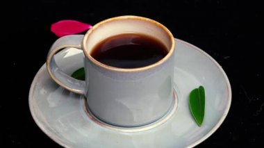 4k video yeşil yaprak ve kırmızı gül yaprağı ile siyah arka plan üzerinde bir kaşık ile mavi bir kahve fincanı yakın kaşık koyarak