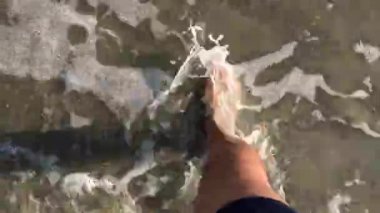 4k video Man ayakları sakin dalgalar ezme veya kumlu plajda sıçrama ile kıyıda yürüyüş. Üstte görüntü