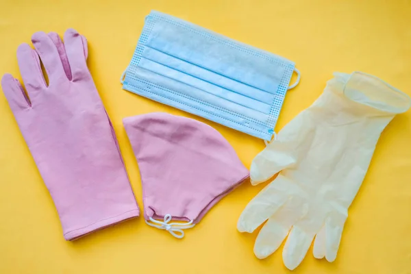 cotton pink gloves and mask with medical gloves and mask on a yellow background. Coronavirus concept