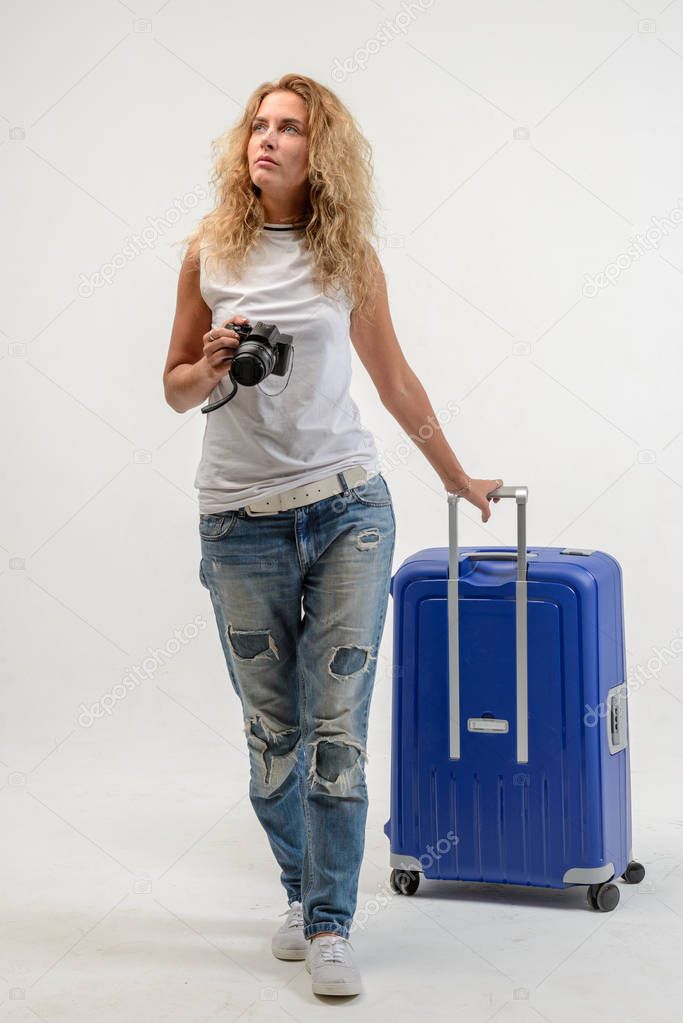 Beautiful young blonde woman with blue plastic suitcase on white background