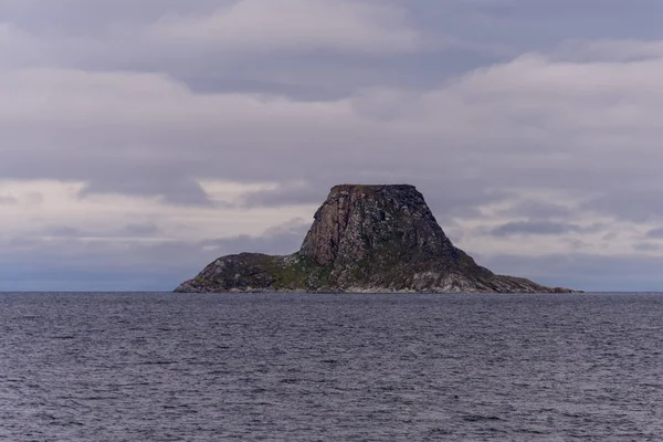 Rock under cloudy sky in ocean water