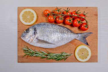 Kiraz domates, biberiye ve limon ahşap kesme tahtası üzerinde taze dorado balık