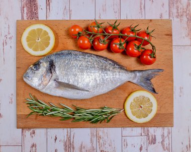 Kiraz domates, biberiye ve limon ahşap kesme tahtası üzerinde taze dorado balık