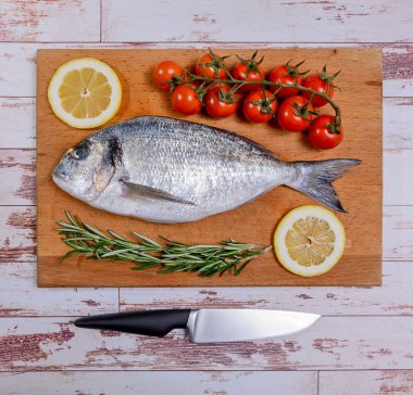 Kiraz domates, biberiye ve limon ahşap kesme tahtası üzerinde taze dorado balık