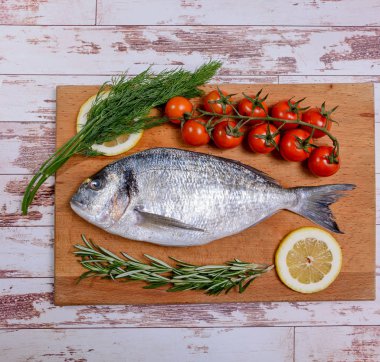 Kiraz domates, biberiye ve limon ahşap kesme tahtası üzerinde taze dorado balık