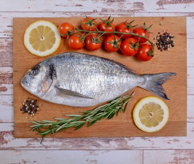 Kiraz domates, biberiye ve limon ahşap kesme tahtası üzerinde taze dorado balık