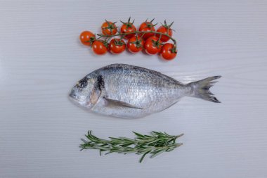 Taze dorada balıkla kiraz domates, biberiye hafif ahşap zemin üzerine