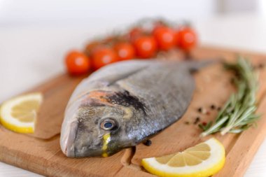 Kiraz domates, biberiye, limon ve biber ahşap kesme tahtası üzerinde taze dorado balık