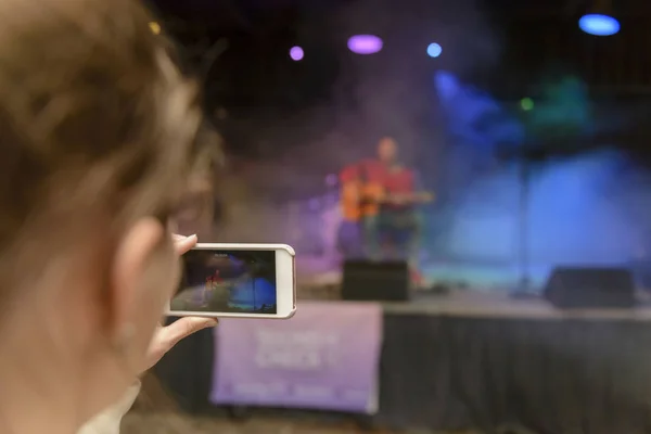 Close-up of unrecognizable woman filming stage concert on mobile phone